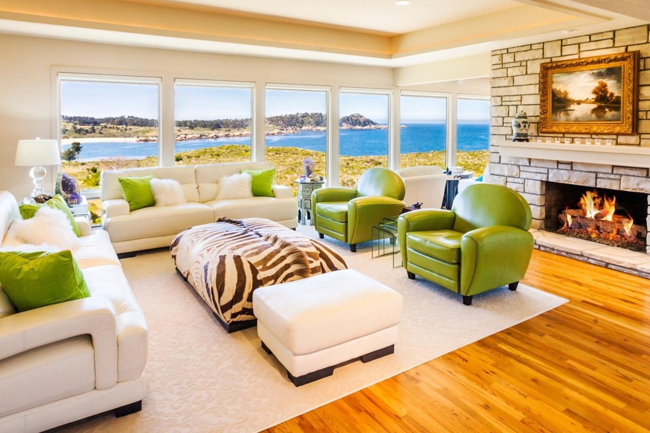 Living room with a stone fireplace, green armchairs, and wide ocean-view windows.