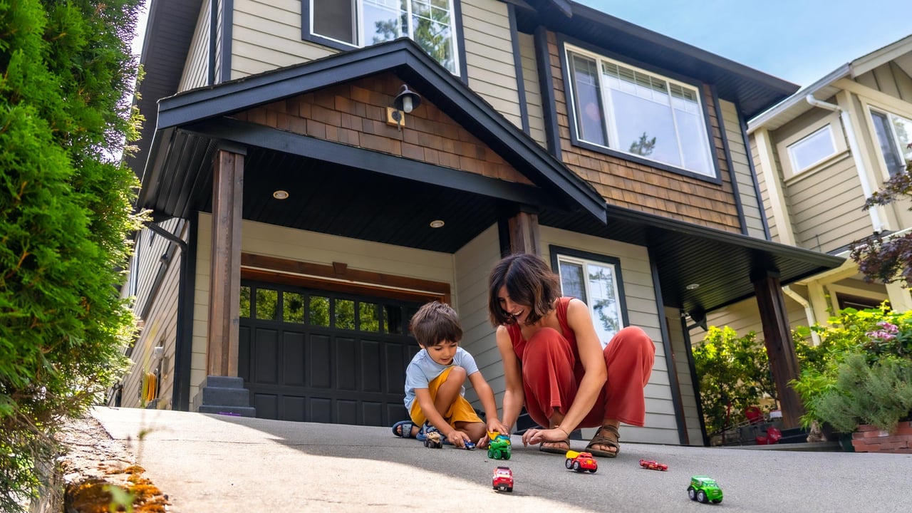 A mother and son playing with toy cars on the spacious driveway of a beautiful suburban home, illustrating the premium lifestyle benefits of moving from Toronto to the suburbs in the West GTA