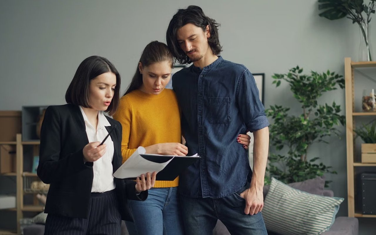 A real estate agent reviews paperwork with a couple in a living room.