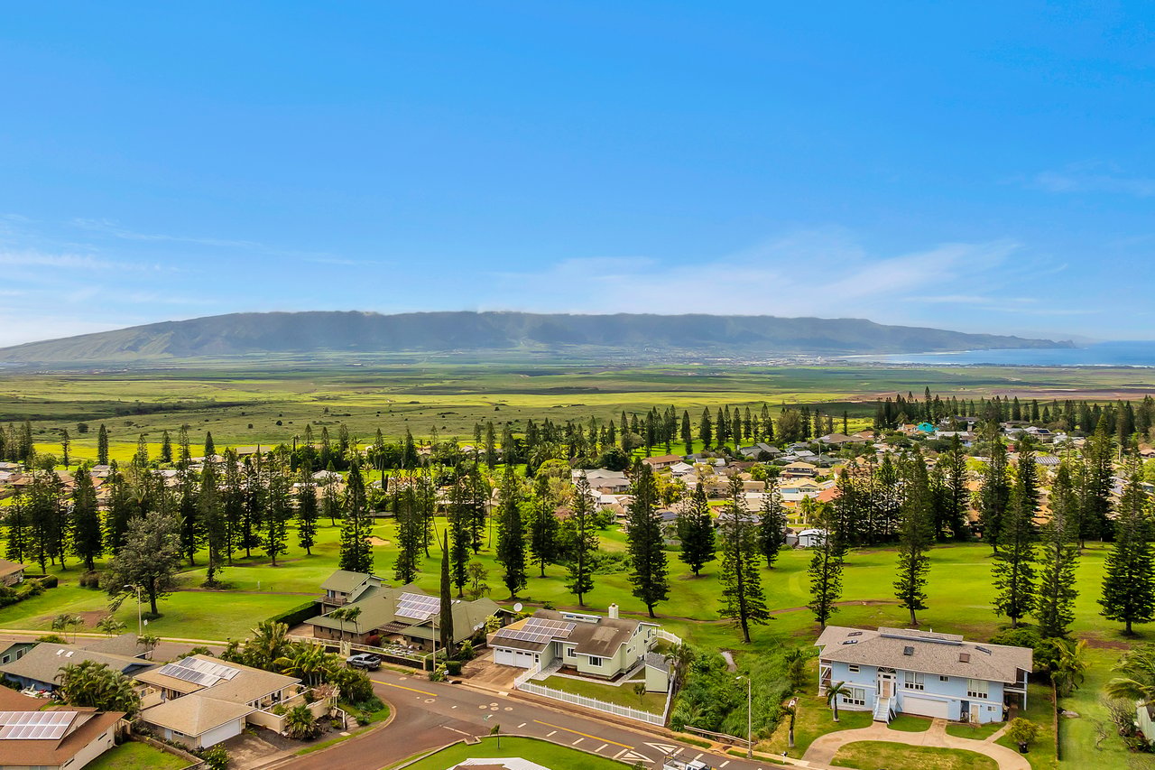 Maui neighborhood and golf course with fields, mountains, and ocean in the distance.