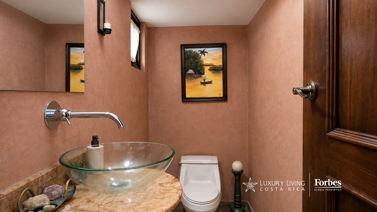 Powder room with a glass vessel sink, stone countertop, white toilet, and terracotta walls.