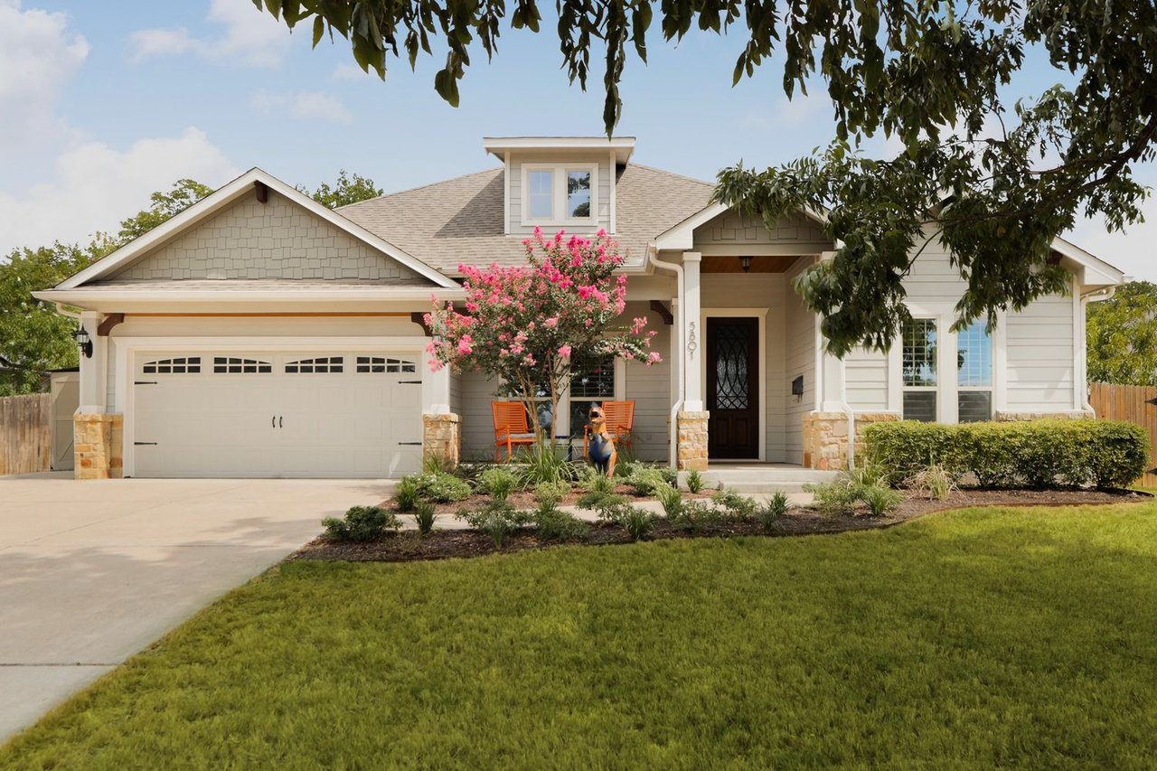 Light-colored house with a two-car garage, flowering tree, and landscaped front lawn.