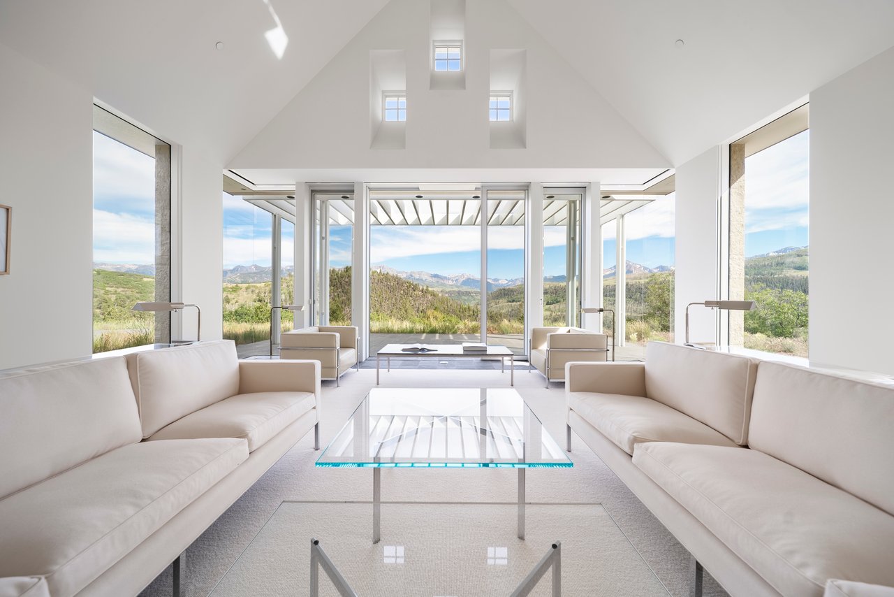 Modern living room with vaulted ceiling, white sofas, and mountain views through expansive windows.