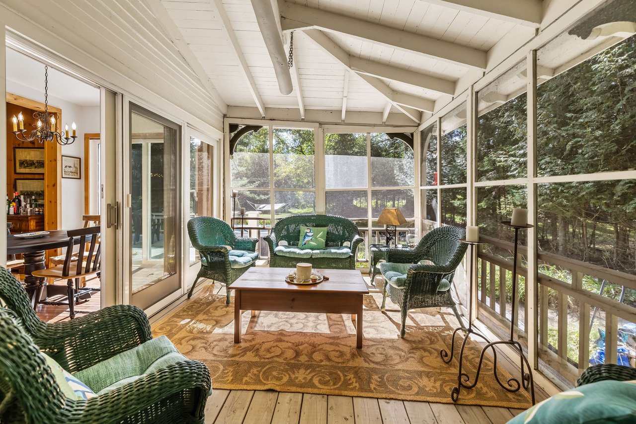 Screened porch with green wicker seating and views of leafy woods.
