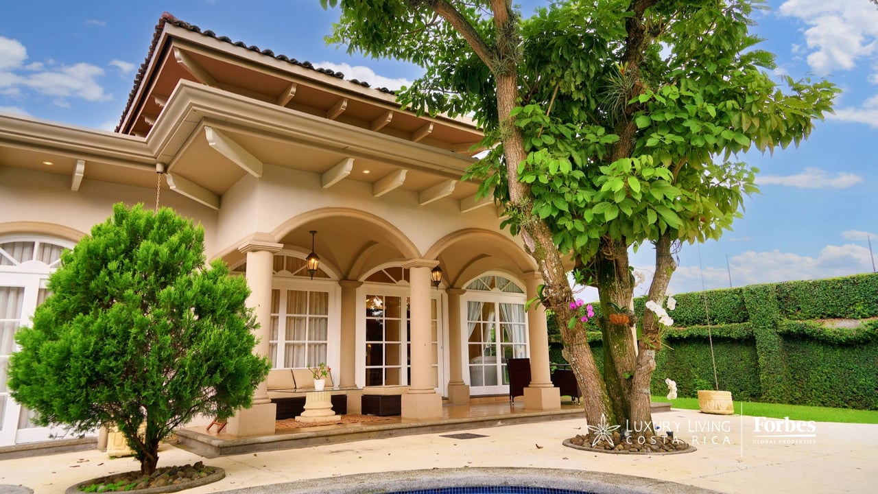 Elegant cream home with arched windows, covered patio, landscaped garden, and pool in the foreground.