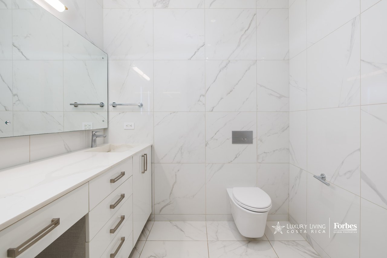 Modern bathroom with white marble-look tile, a long vanity, and a white toilet.