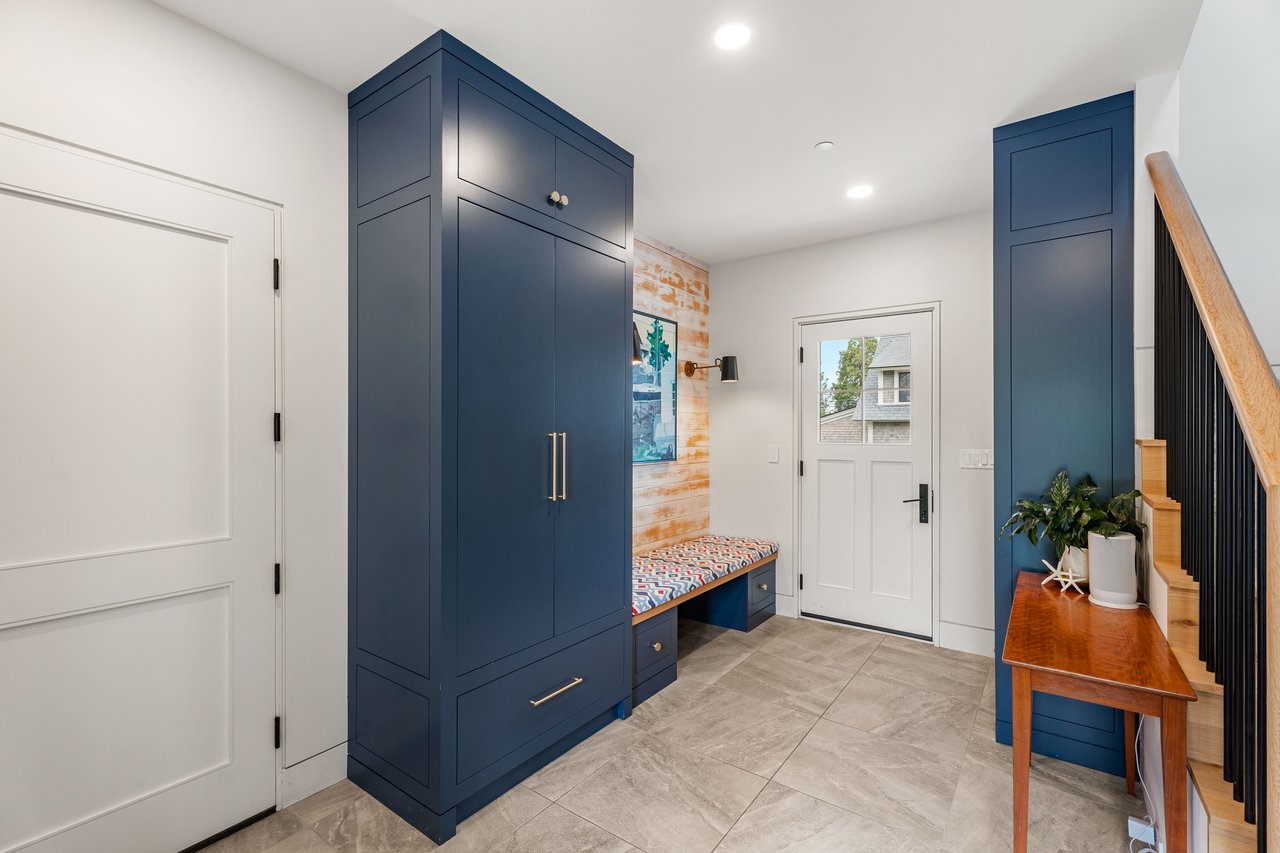 Entryway with navy built-in cabinets, a patterned bench, and a staircase with a wood handrail.