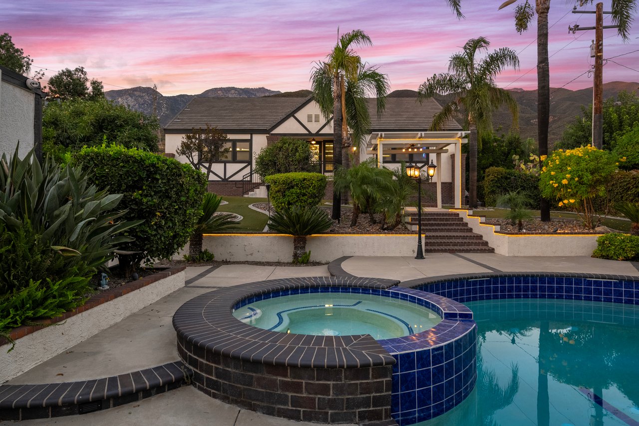 Custom home with a swimming pool and raised circular spa, palm trees, and mountains at dusk.
