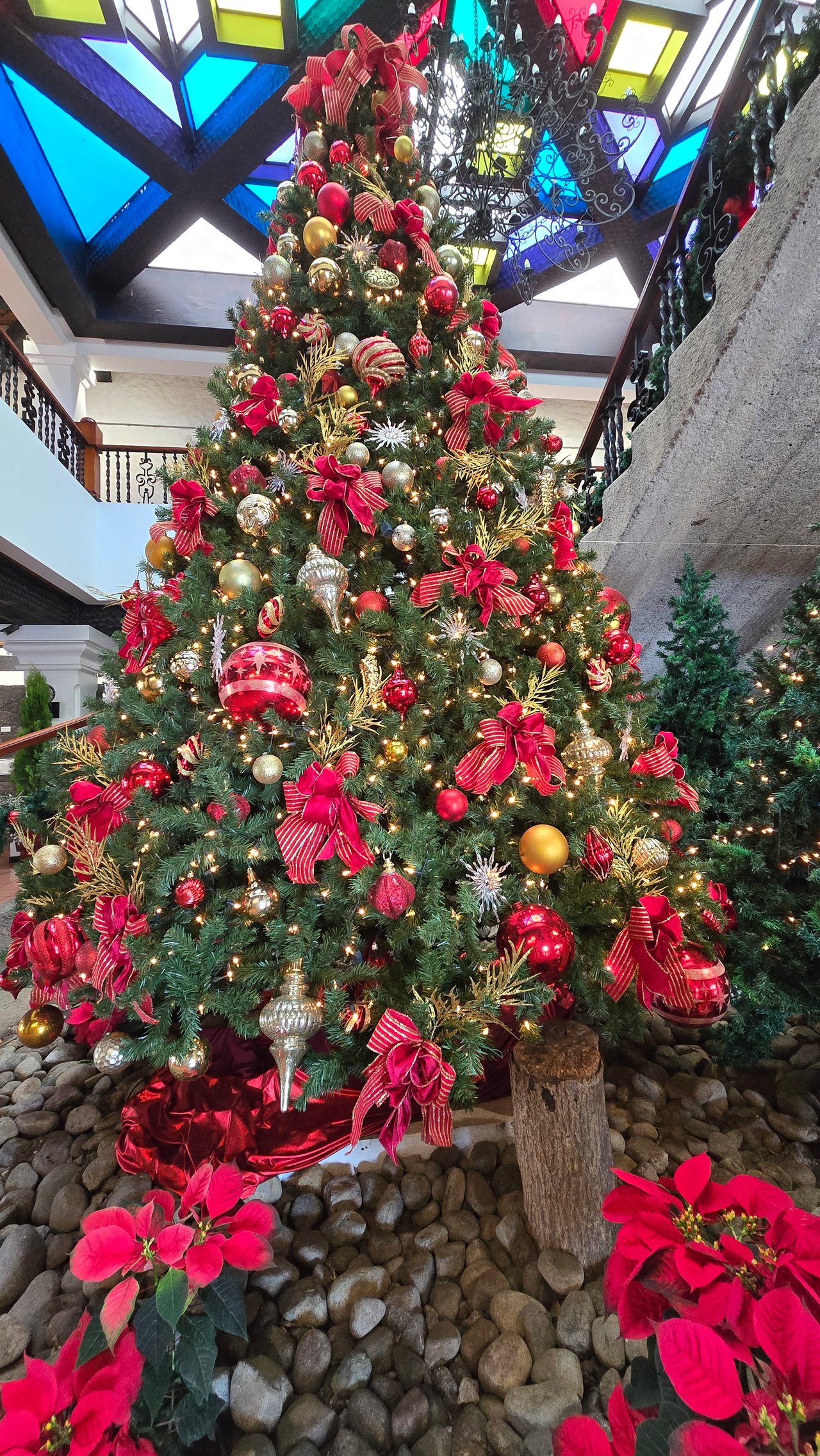 Christmas tree with red and gold decorations beneath a colorful stained-glass atrium ceiling