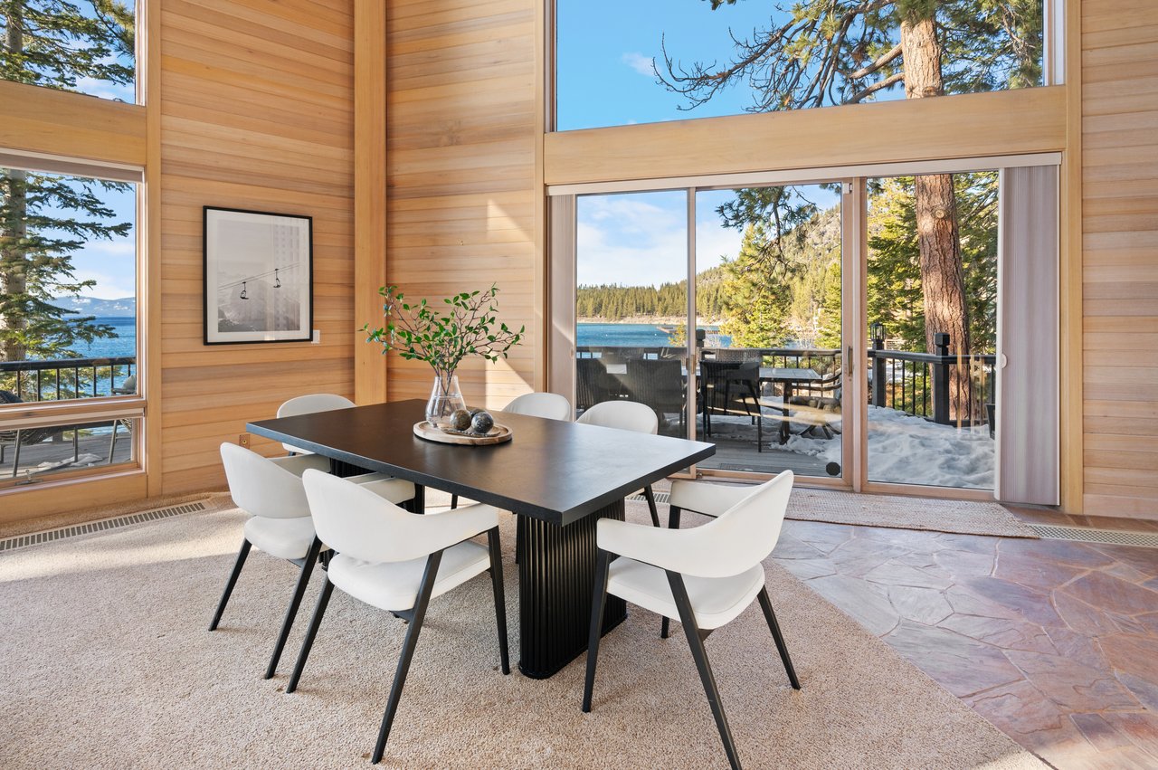 Dining area with a black table and white chairs, looking out through large windows to the lake.