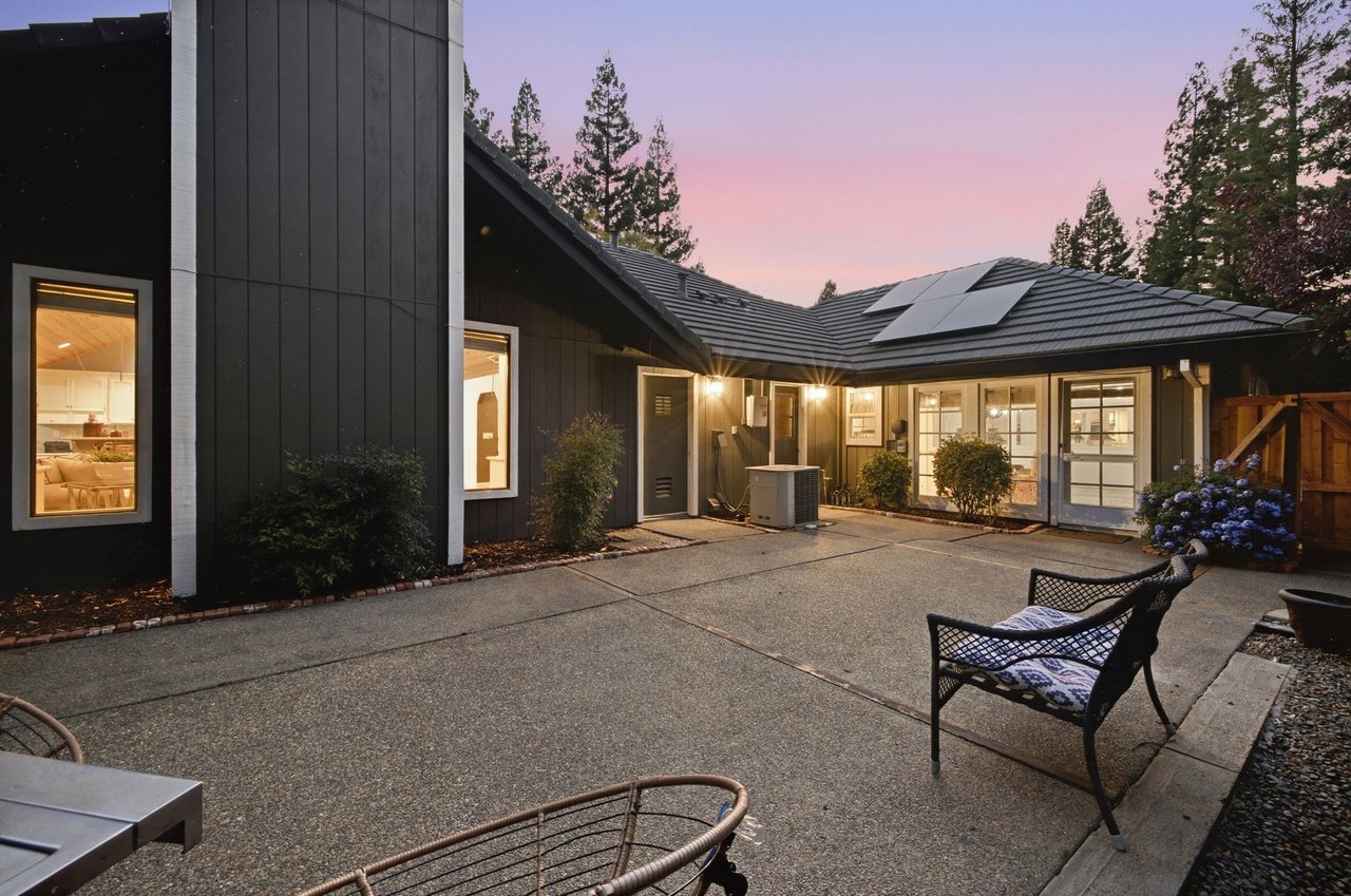 Rear exterior of a dark-sided home with solar panels and a paved patio at dusk.