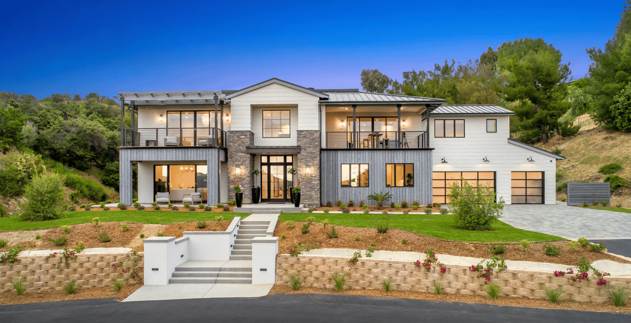 Modern two-story home with stone accents, balconies, landscaped lawn, and attached garage.