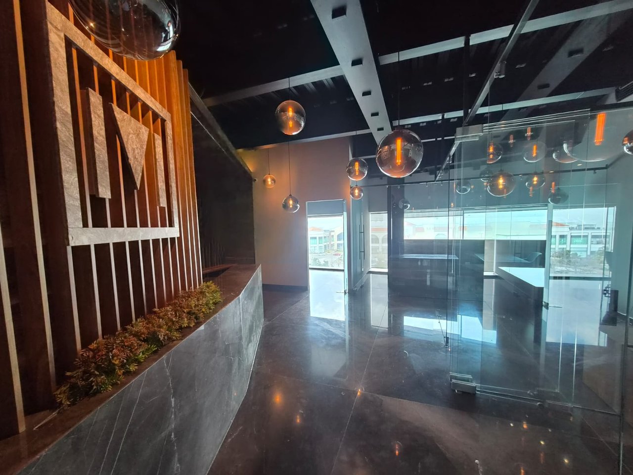 Modern office reception with glass partitions, globe pendant lights, and a wood-slat planter wall.