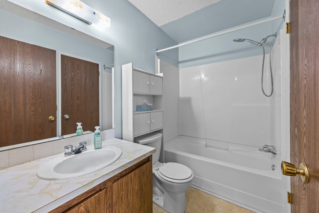 Bathroom with a wood vanity, mirrored wall, toilet, and white tub-shower.