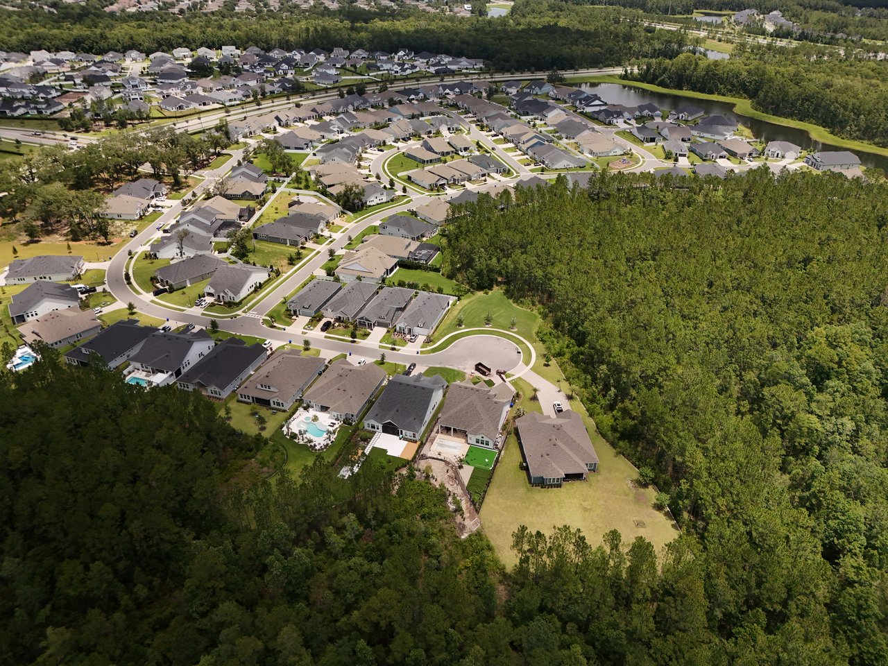 Aerial view of homes along winding streets, bordered by woodland and a pond.