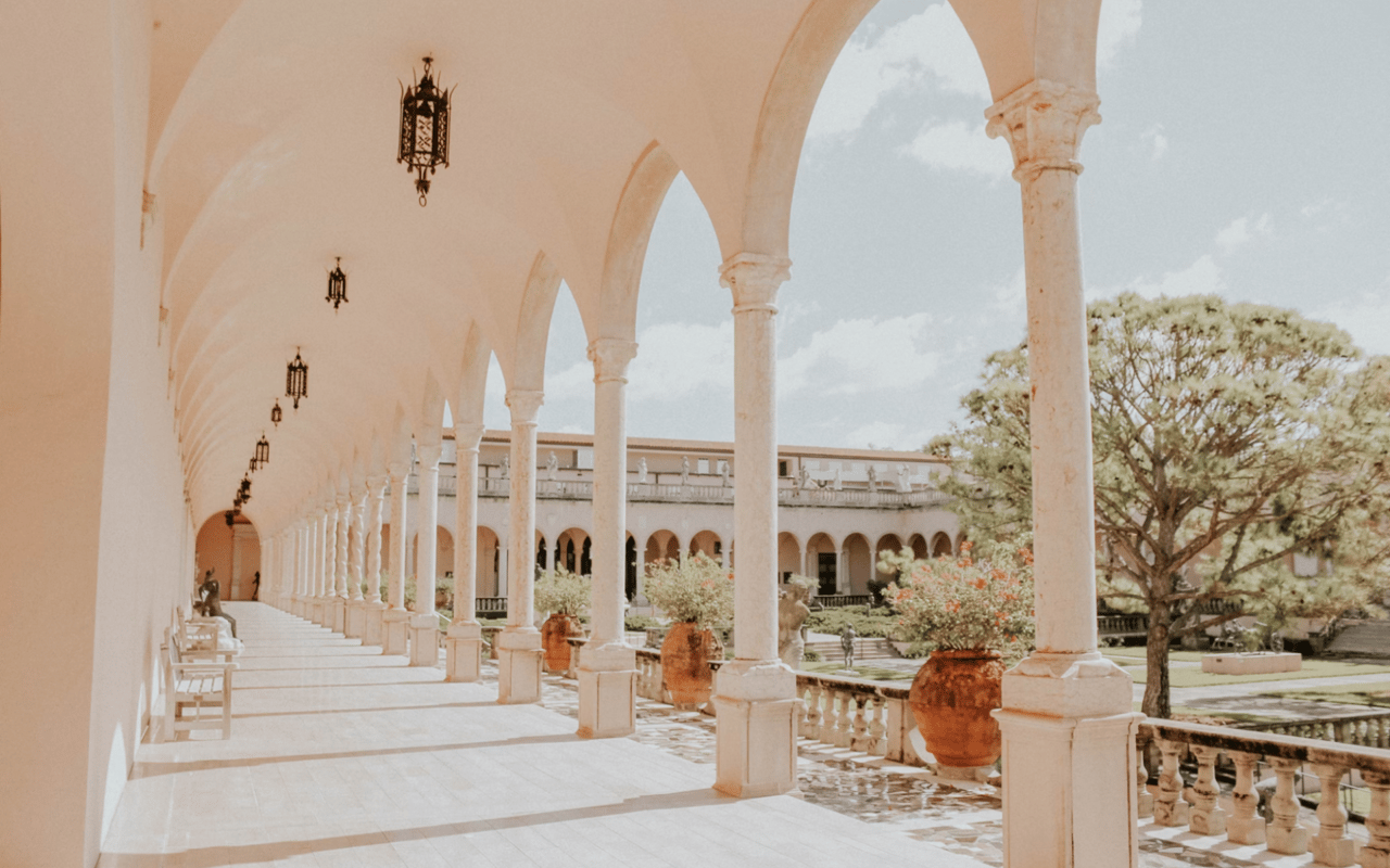  A long, arched loggia with tall, light-colored columns stretches into the distance on the left, leading to an ornate building in the background.