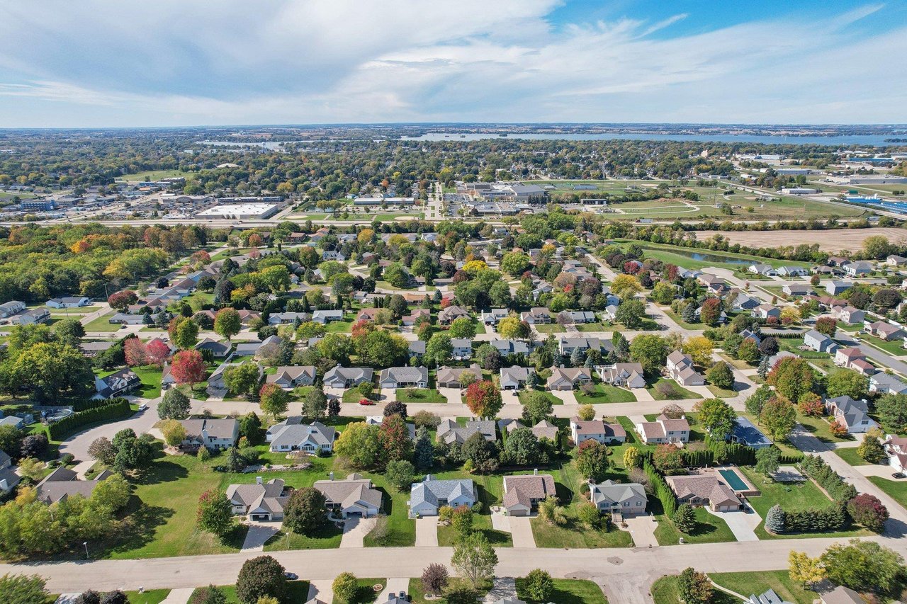 Aerial view of a Beaver Dam, Wisconsin neighborhood with homes, tree-lined streets, and water in the distance.