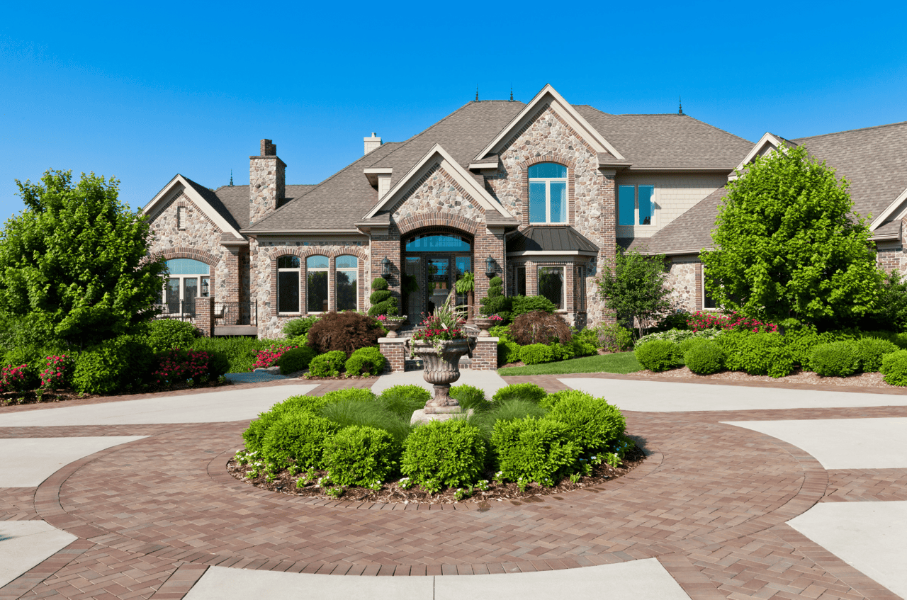 A large brick house with a circular driveway and a fountain in front of it.