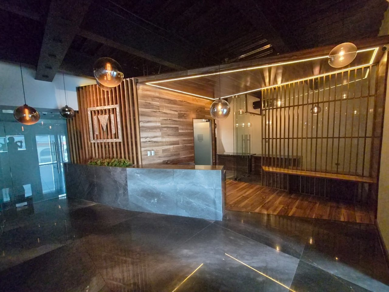 Modern office reception lobby with a dark stone desk, wood paneling, and globe pendant lights.