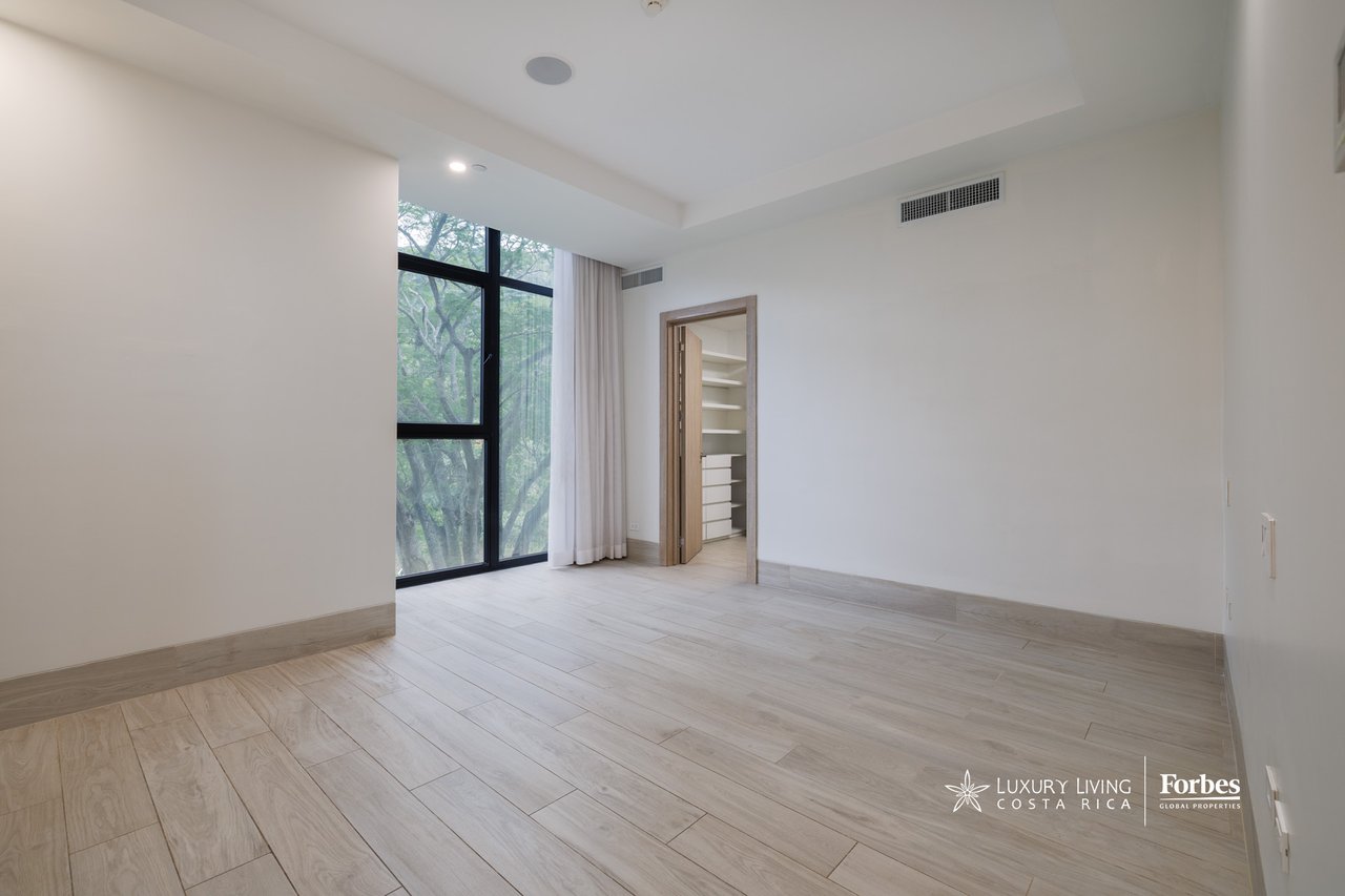 Unfurnished bedroom with pale tile floors, a large tree-facing window, and an open closet.