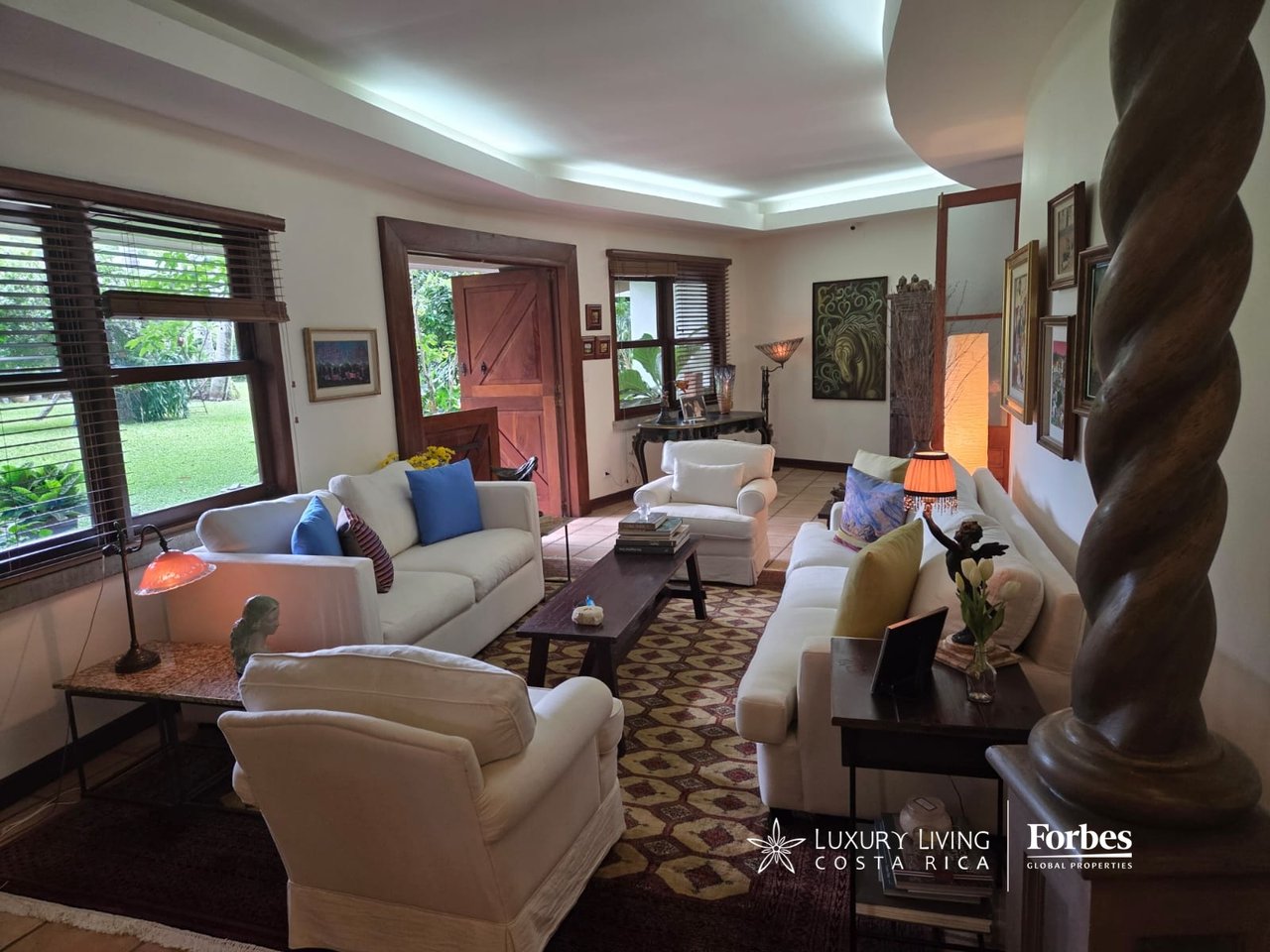 Living room with white sofas, a patterned rug, and windows overlooking a garden.