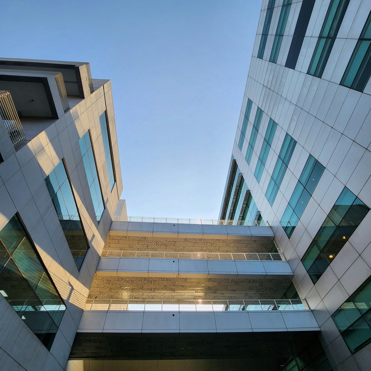 Modern glass buildings connected by skybridges, viewed from below against a clear blue sky.