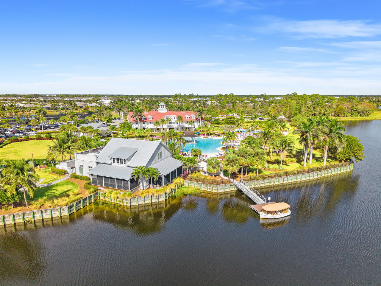 Waterfront property with a gray-roofed building, palm-lined grounds, a pool, and a boat.