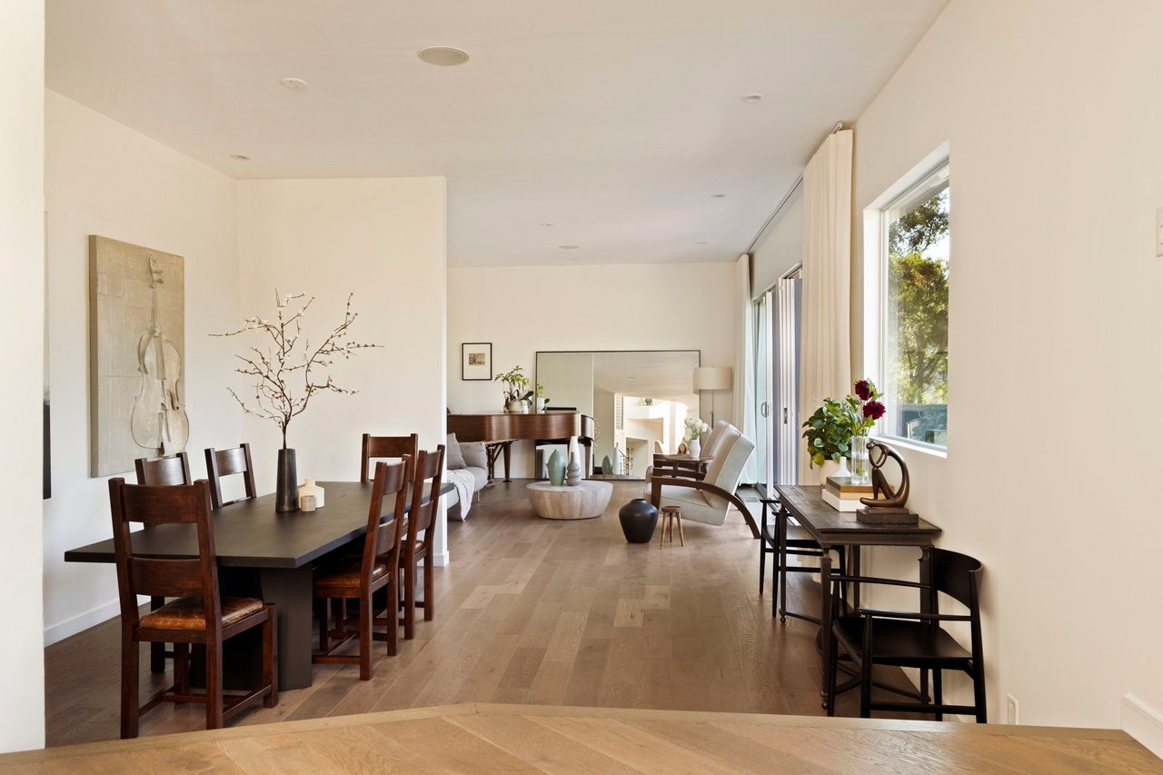 Open-plan dining and living room with a dark wood dining table, piano, and tall windows.