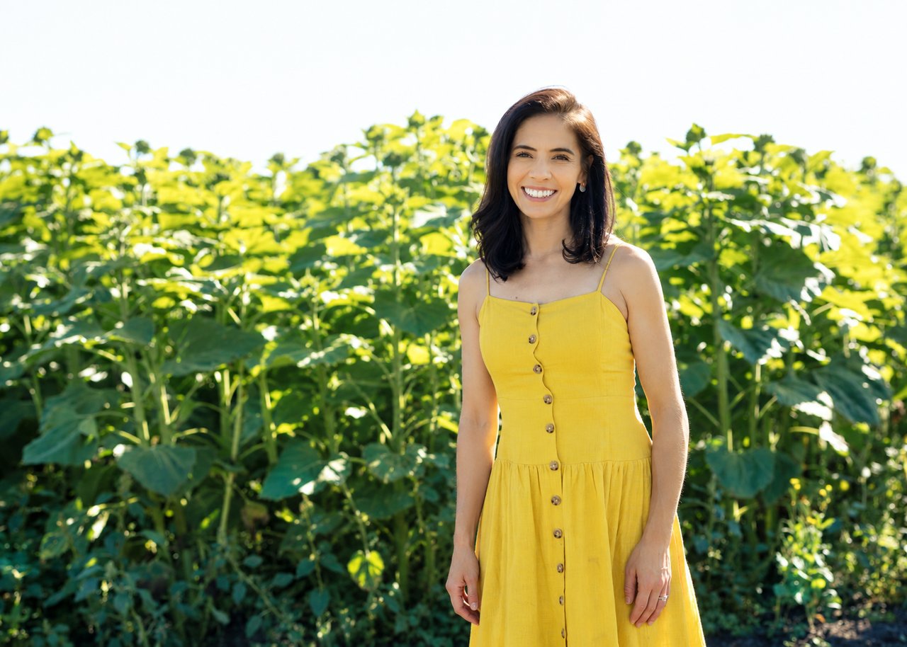 Ashley McDonald smiling in a yellow dress in a sunlit garden.