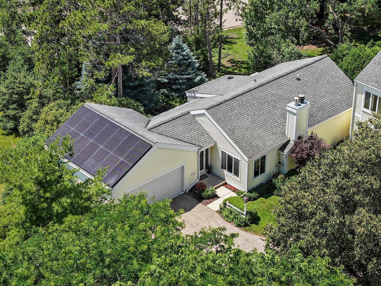 An aerial view of a Madison-area home with a rooftop solar array surrounded by mature trees, an example of a residential energy-efficiency upgrade.