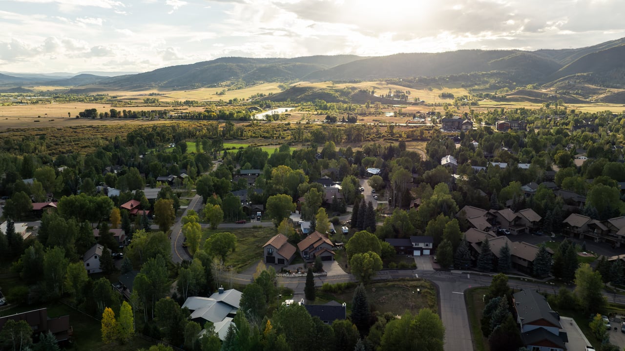 Aerial view of a residential neighborhood with distant open fields and mountain ridges.