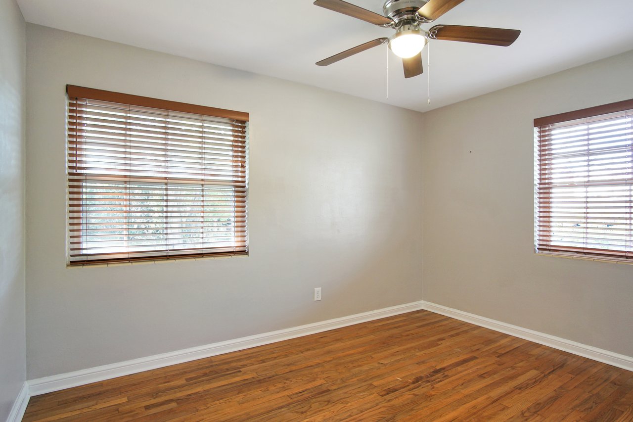 An empty room featuring a ceiling fan and two windows allowing natural light to enter.