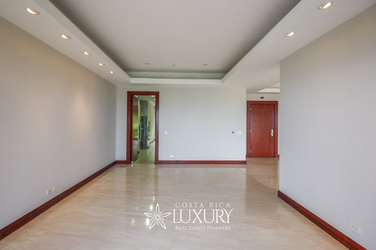 Vacant apartment living room with polished tile floors, recessed ceiling lights, and dark wood trim.