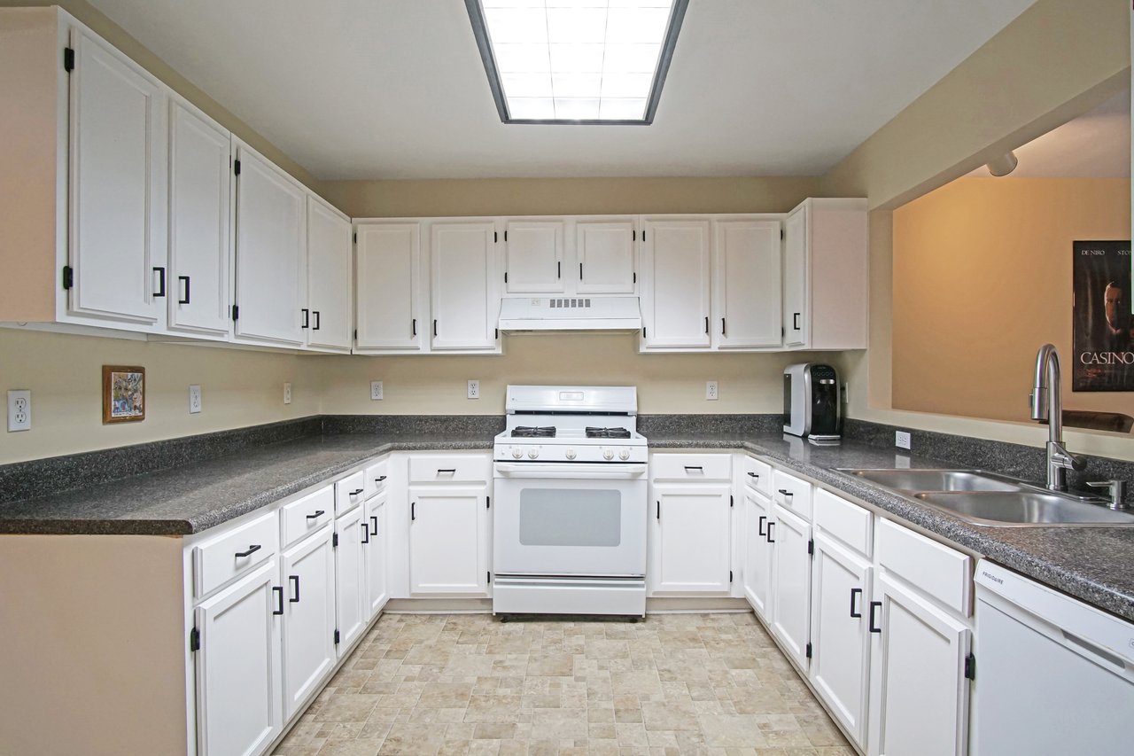 Kitchen at 529 Collinsford Road, Tallahassee, Florida, featuring ample white cabinetry with black hardware, gray countertops, and a gas range with a white hood. The room includes a double sink, dishwasher, and pass-through window to the living area. A large overhead light brightens the space, creating a clean and functional layout.