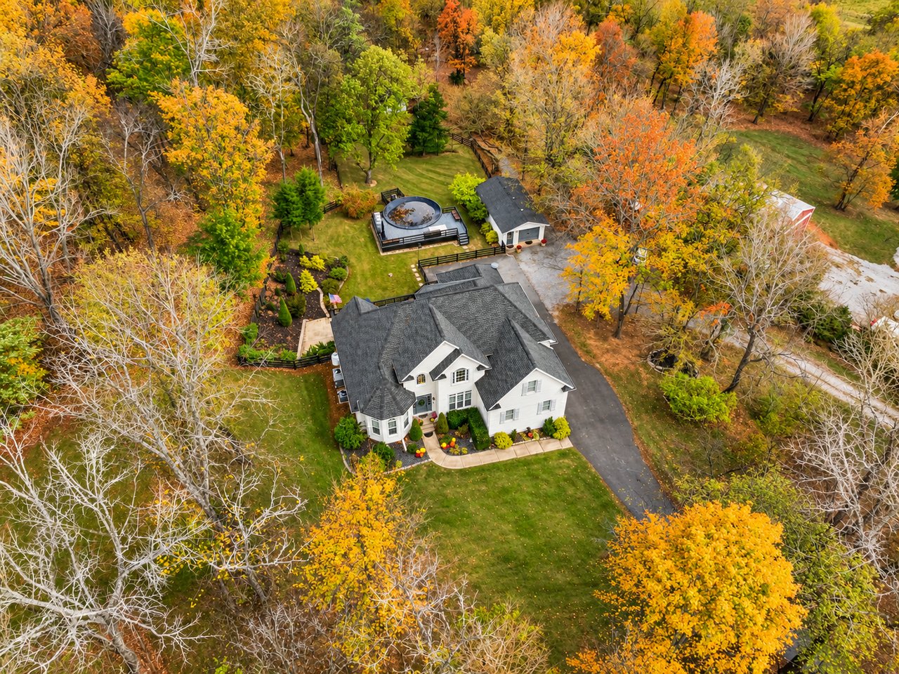 Aerial view of a white house, landscaped grounds, and circular spa amid autumn foliage.