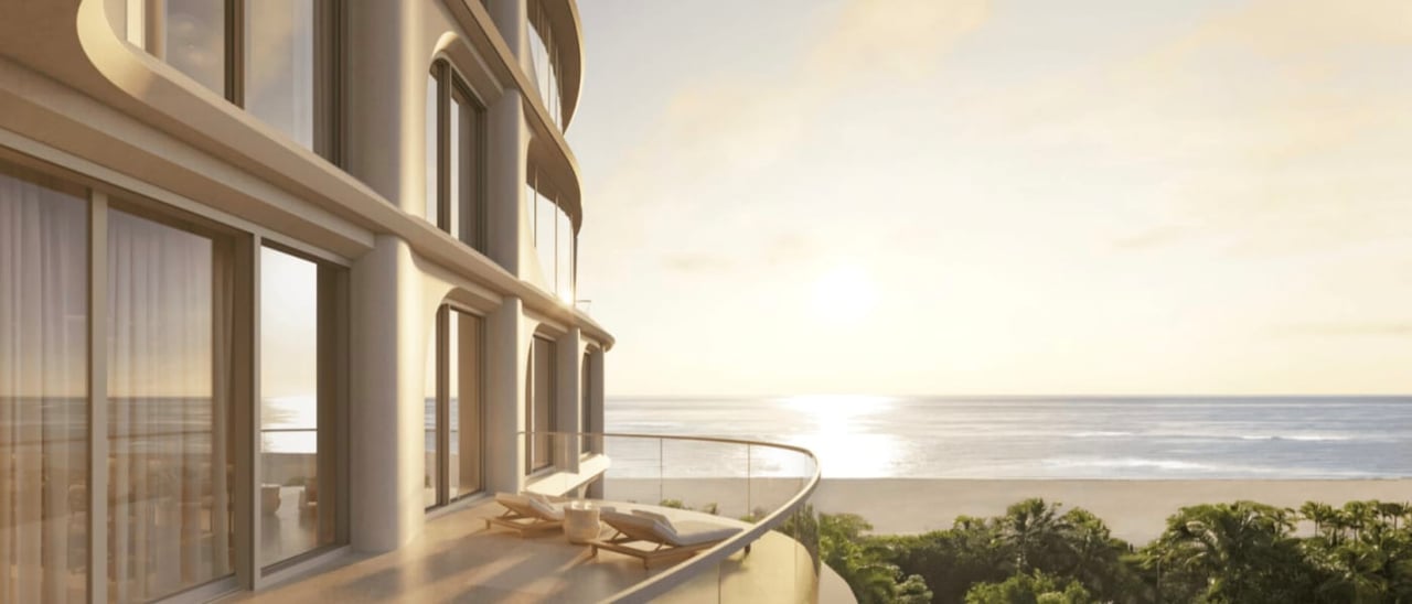 Curved condominium balcony with lounge chairs overlooking the beach and ocean at golden hour.