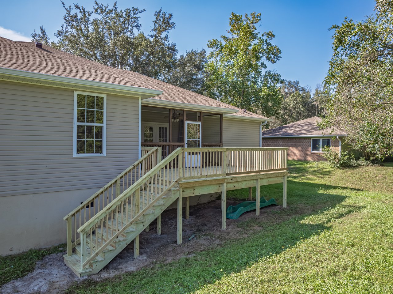 Rear of a light-sided home with a raised wooden deck, long stairs, and screened porch.
