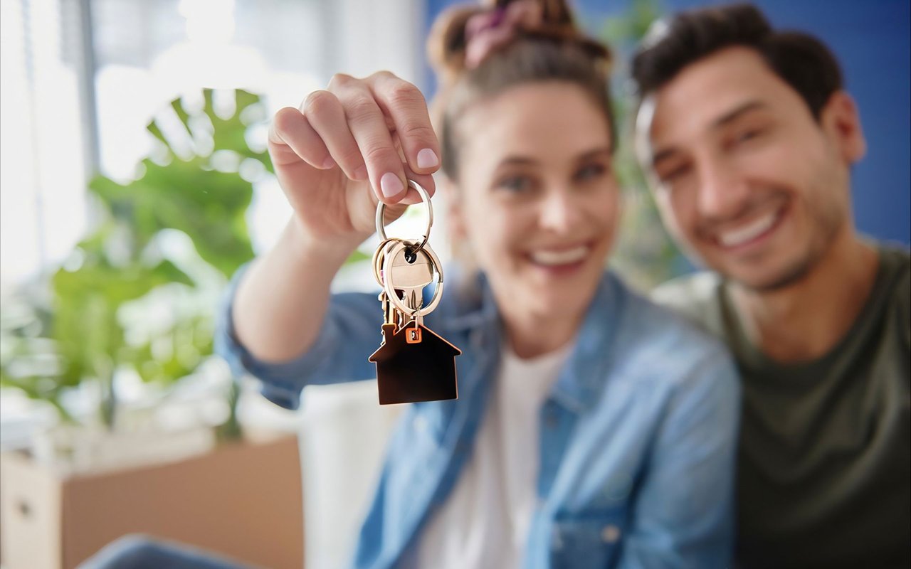 A woman holds up house keys as she and her partner celebrate.