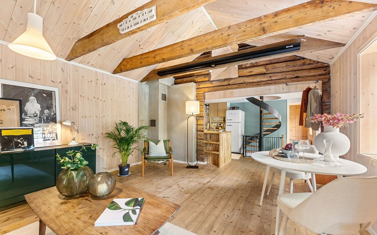 Furnished wood-paneled living area with exposed beams, a compact kitchen, and spiral staircase.