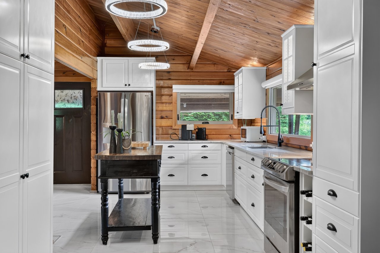 Kitchen with white cabinetry and stainless appliances beneath a vaulted wood-plank ceiling.