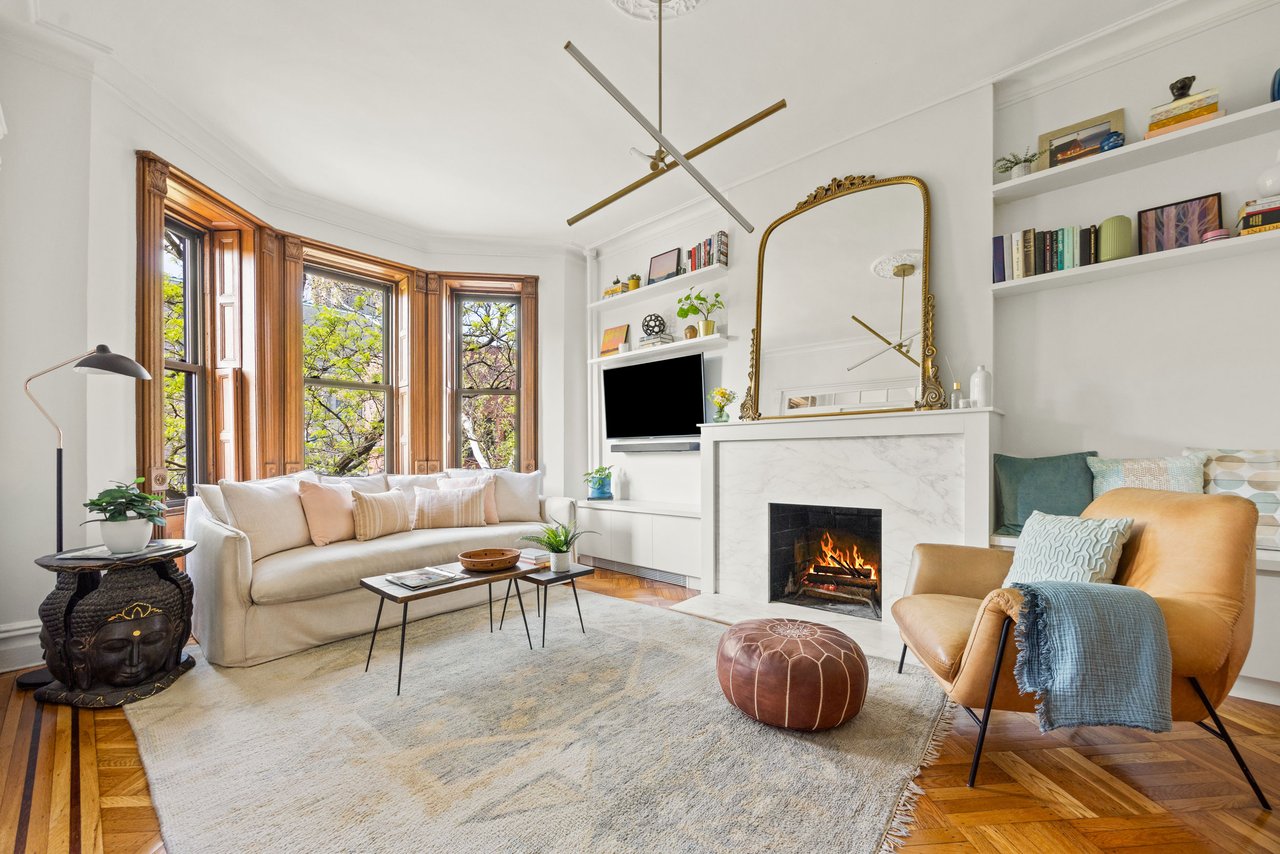 Living room with wood-trimmed bay windows, a marble fireplace, built-in shelves, and parquet floors.