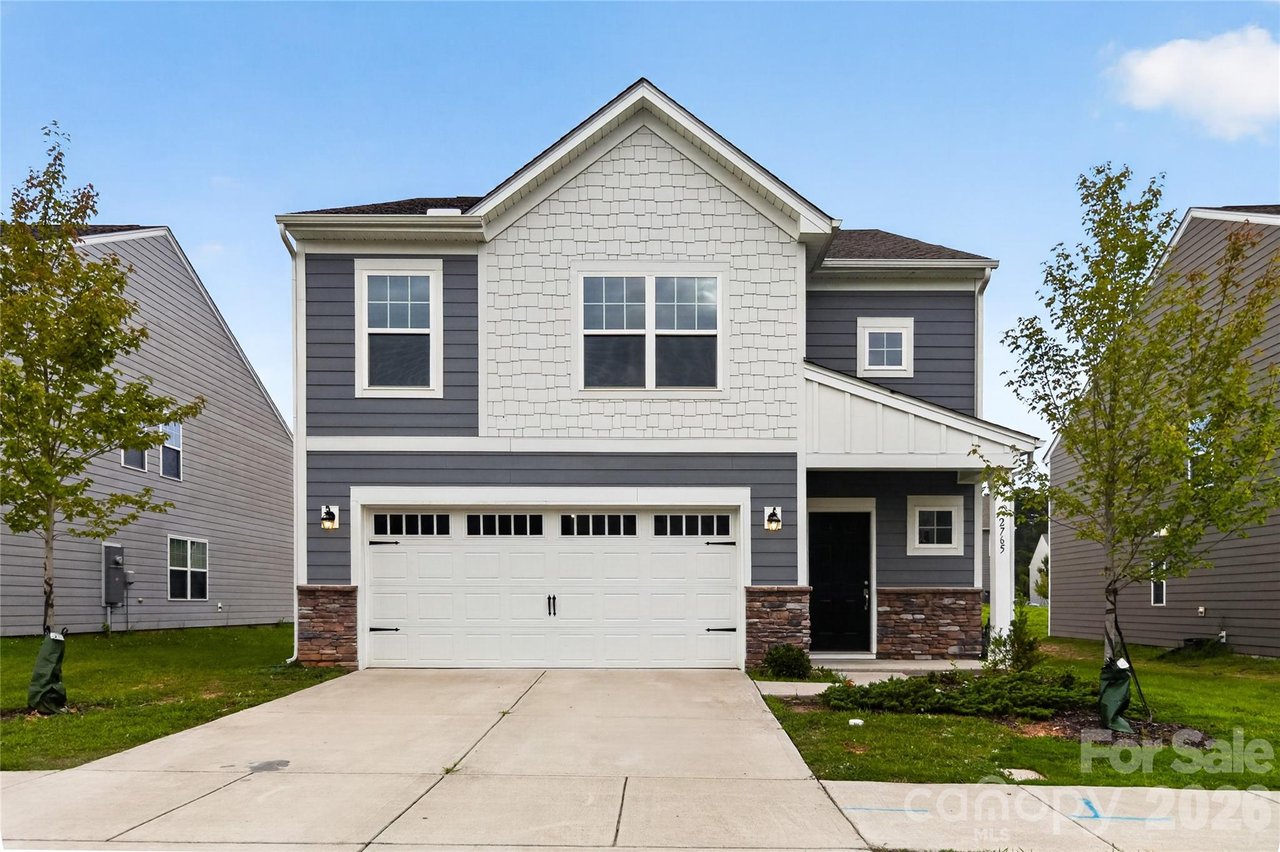 Two-story gray-and-white house with a double garage, stone accents, and a covered front entry.