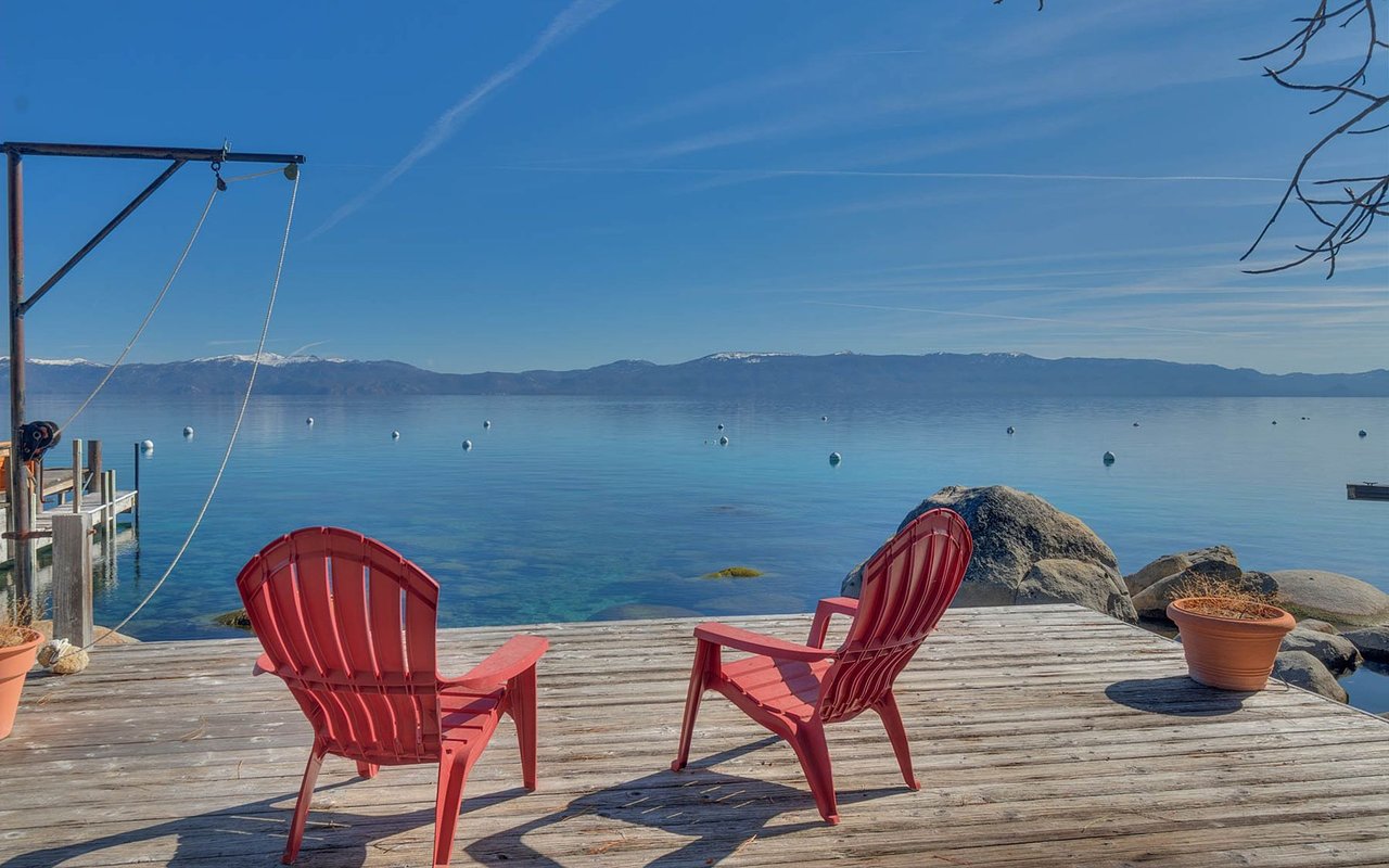 Lakefront deck with two red Adirondack chairs overlooking calm water and distant mountains.