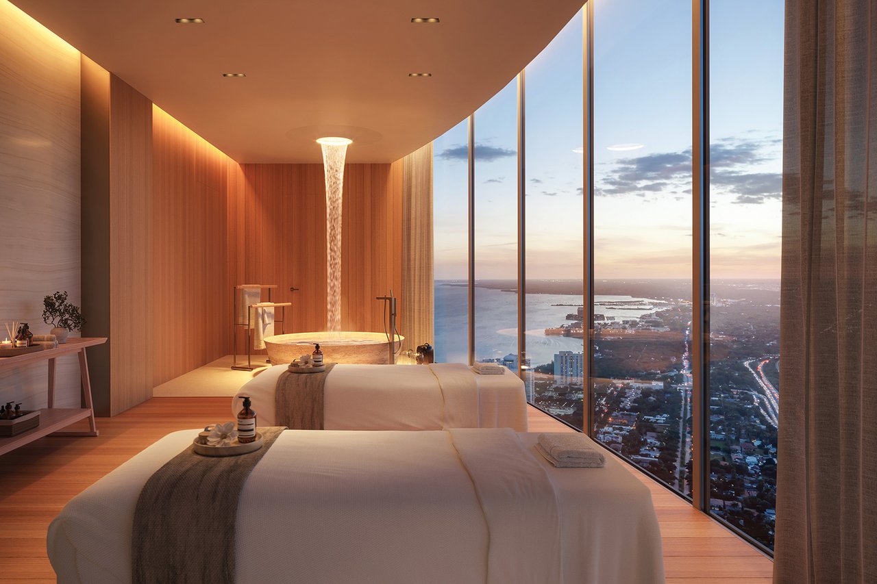 Bedroom with a freestanding tub and floor-to-ceiling windows overlooking water at dusk.