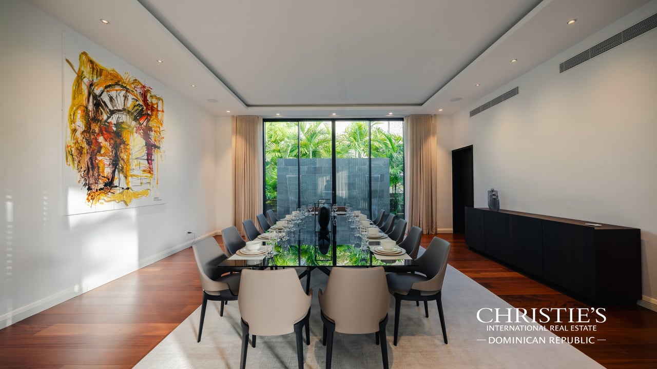 Dining room with a long glass table, sculptural chairs, and garden-facing windows.