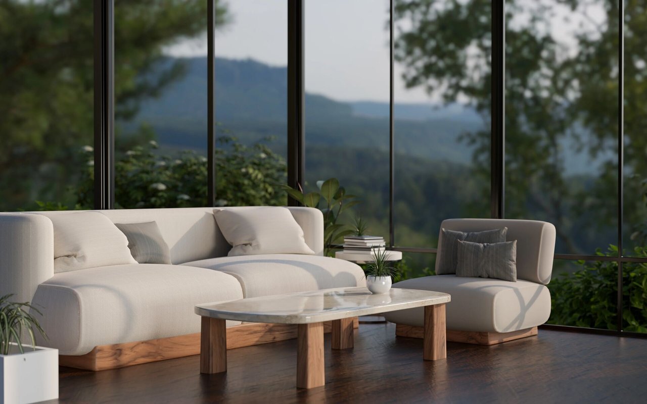 Living room with a cream sectional and armchair facing floor-to-ceiling windows overlooking wooded mountains.