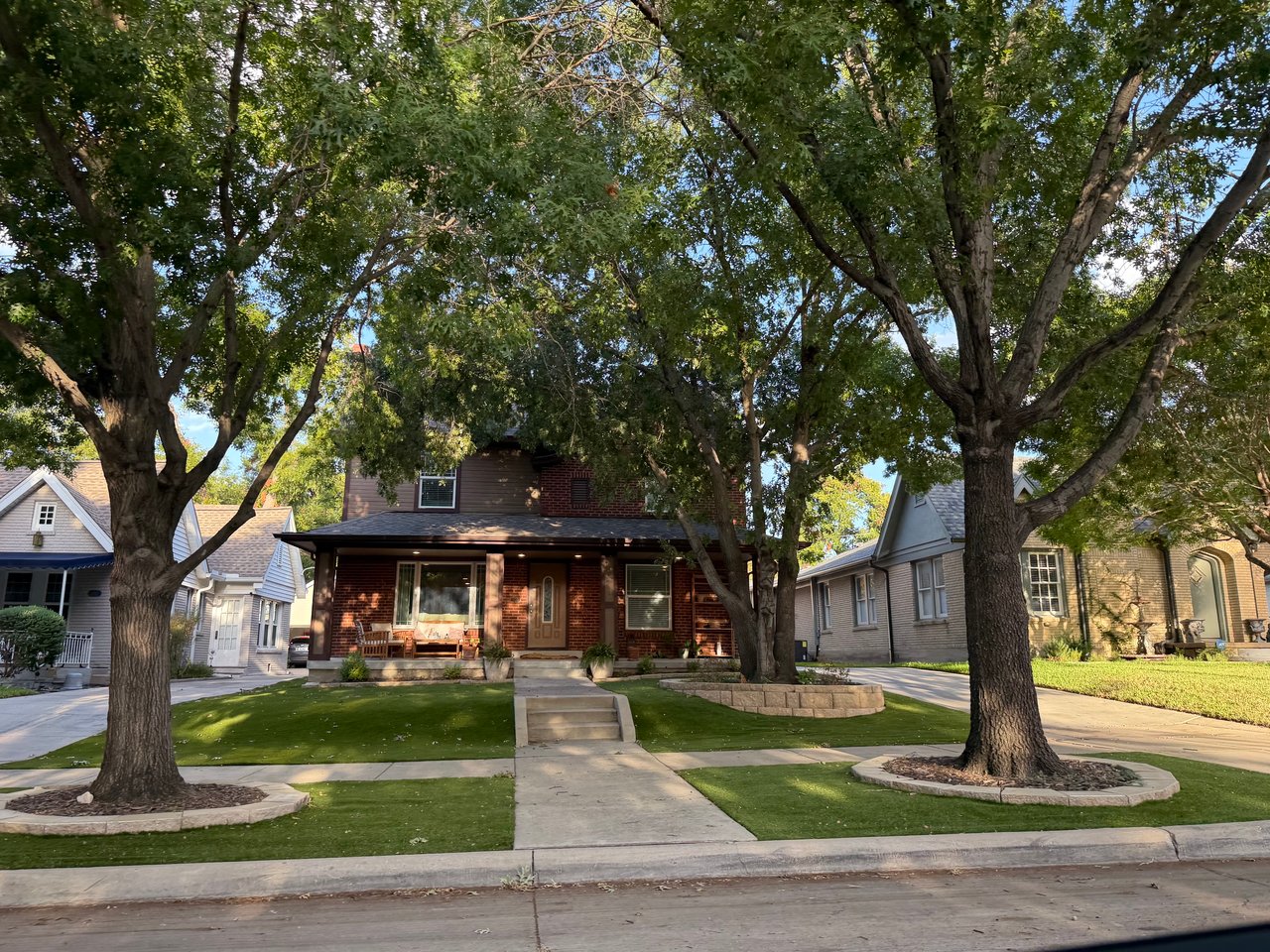 Red-brick two-story Ryan Place home with a covered porch beneath mature trees.