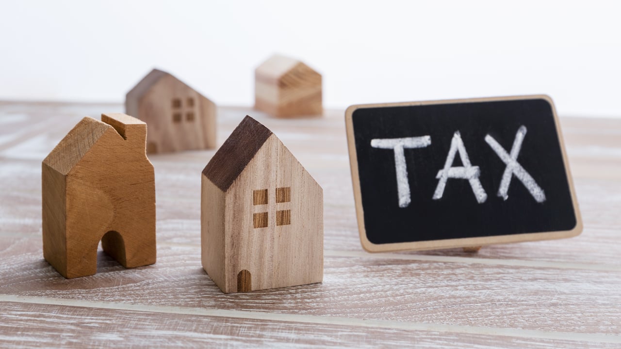 Wooden model houses beside a chalkboard sign reading "TAX" for Macon County NC property tax