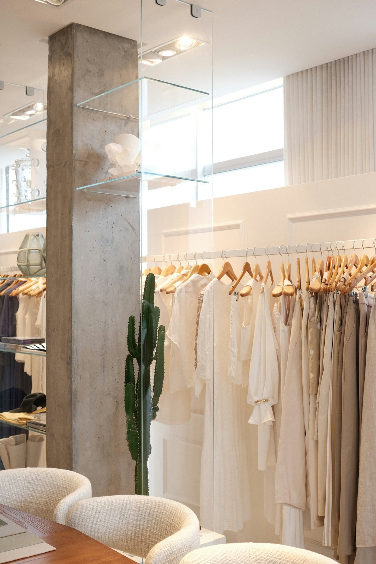 Bright boutique interior with clothing racks, glass shelves, and a concrete column.