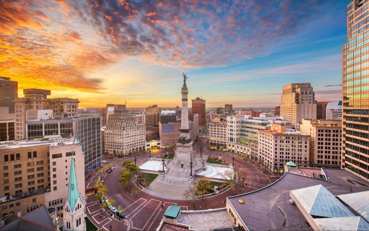 Stunning golden hour drone view of Monument Circle in downtown Indianapolis, showcasing the Soldiers and Sailors Monument, urban architecture, and city streets.